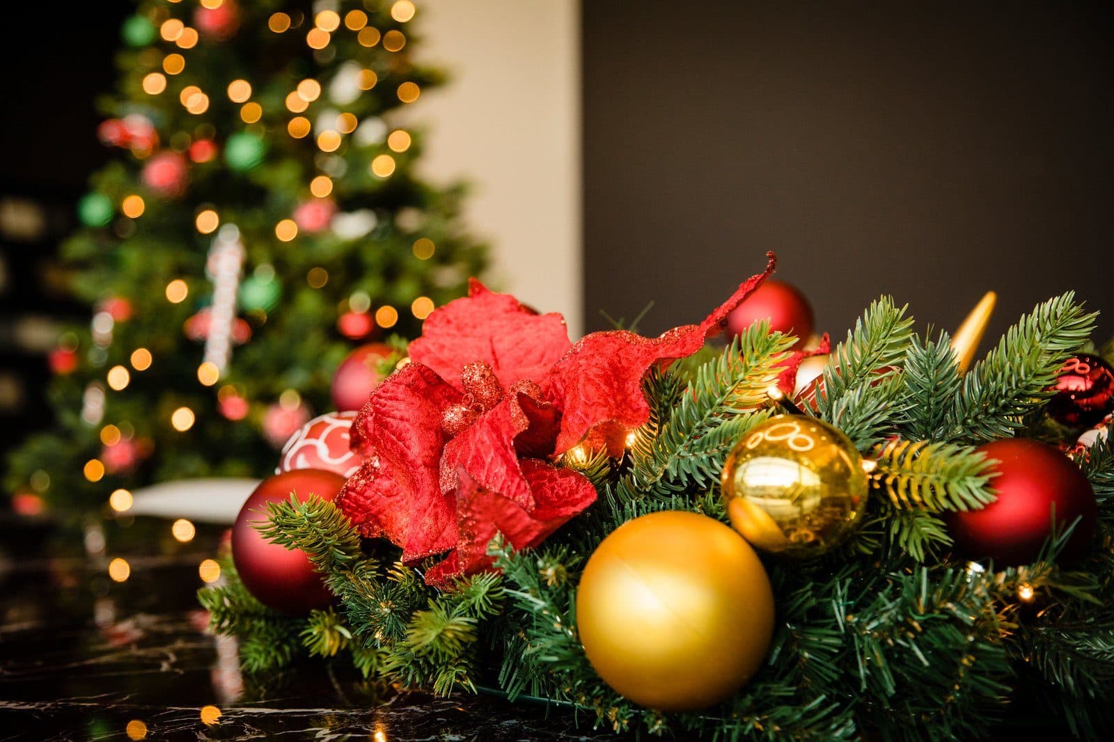Kerststuk met rode bloemen en gouden kerstballen voor een verlichte kerstboom